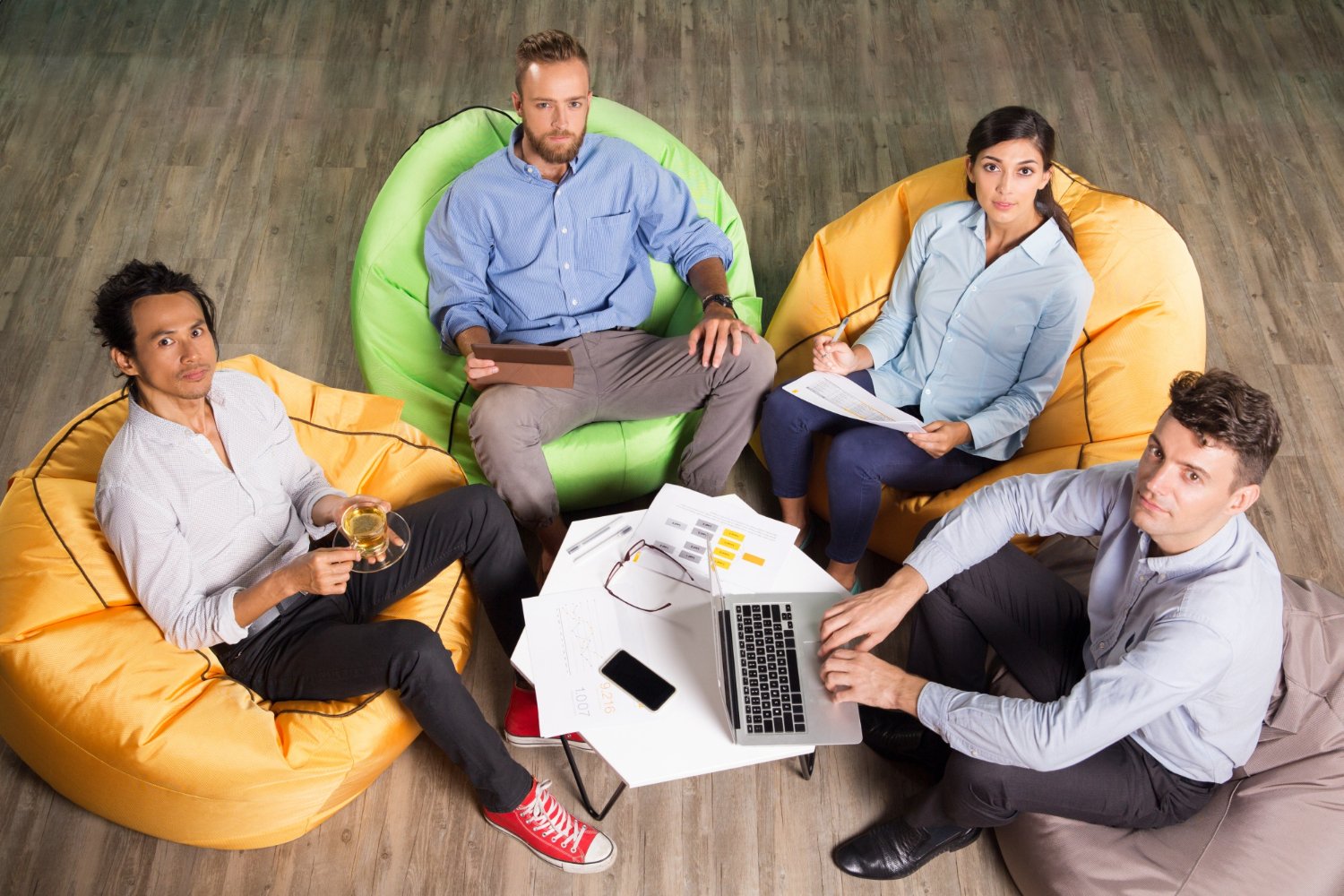 Four business people sitting on beanbag chairs collaborating in a relaxed office setting