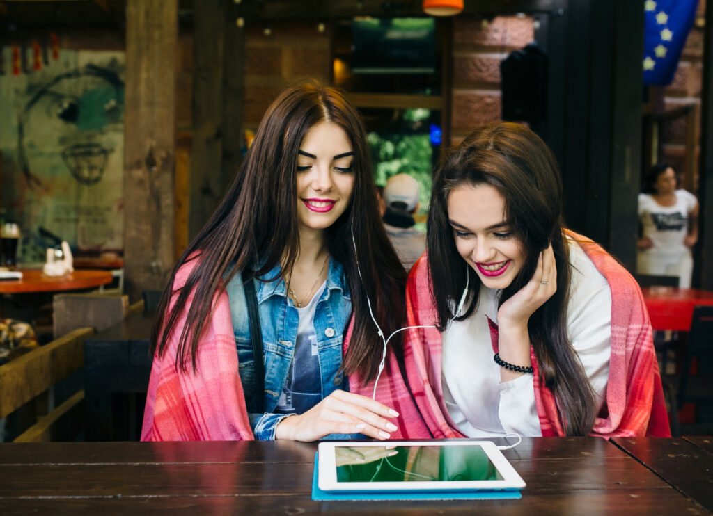 Two young women sitting at a table watching something on a tablet together
