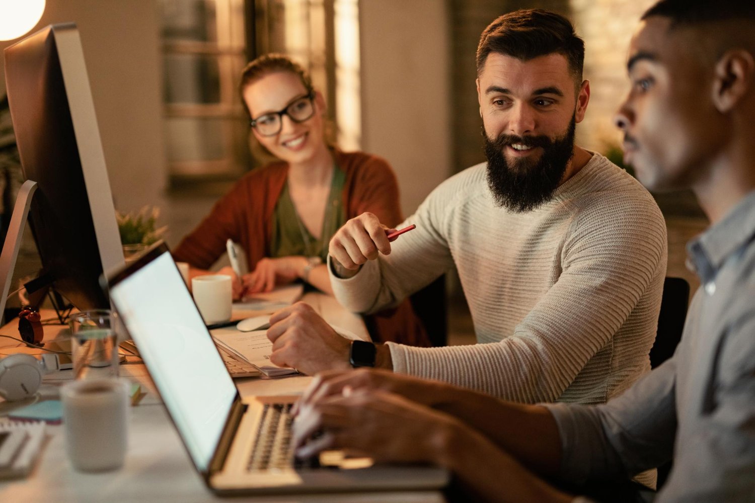 Young freelance workers using laptop while working late in the office with focus on bearded man